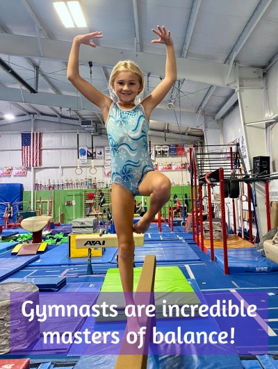 Girl balancing in a scale on beam in gymnastics class