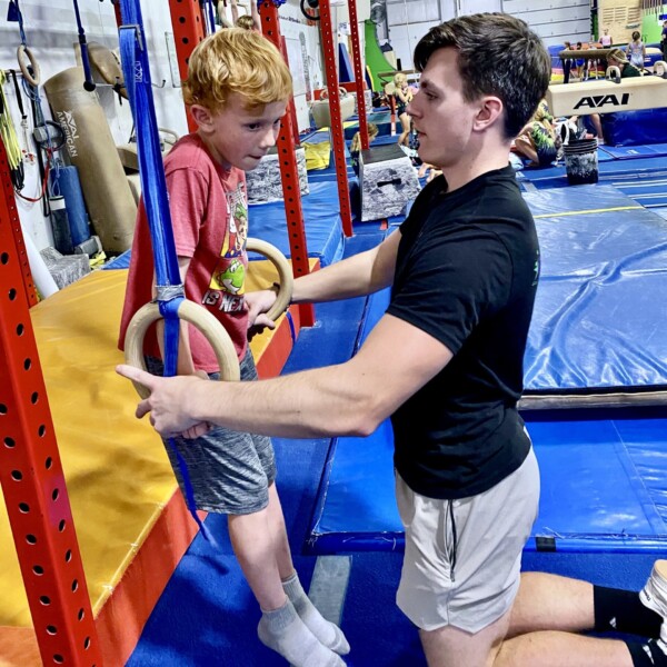 Boys gymnastics coach working with student on rings