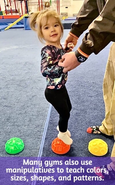 Toddler girl jumping on colored manipulative shapes in gymnastics class Toddler girl jumping on colored manipulative shapes in gymnastics class