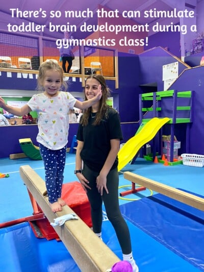 Toddler girl walking on beam with coach nearby Toddler girl walking on beam with coach nearby