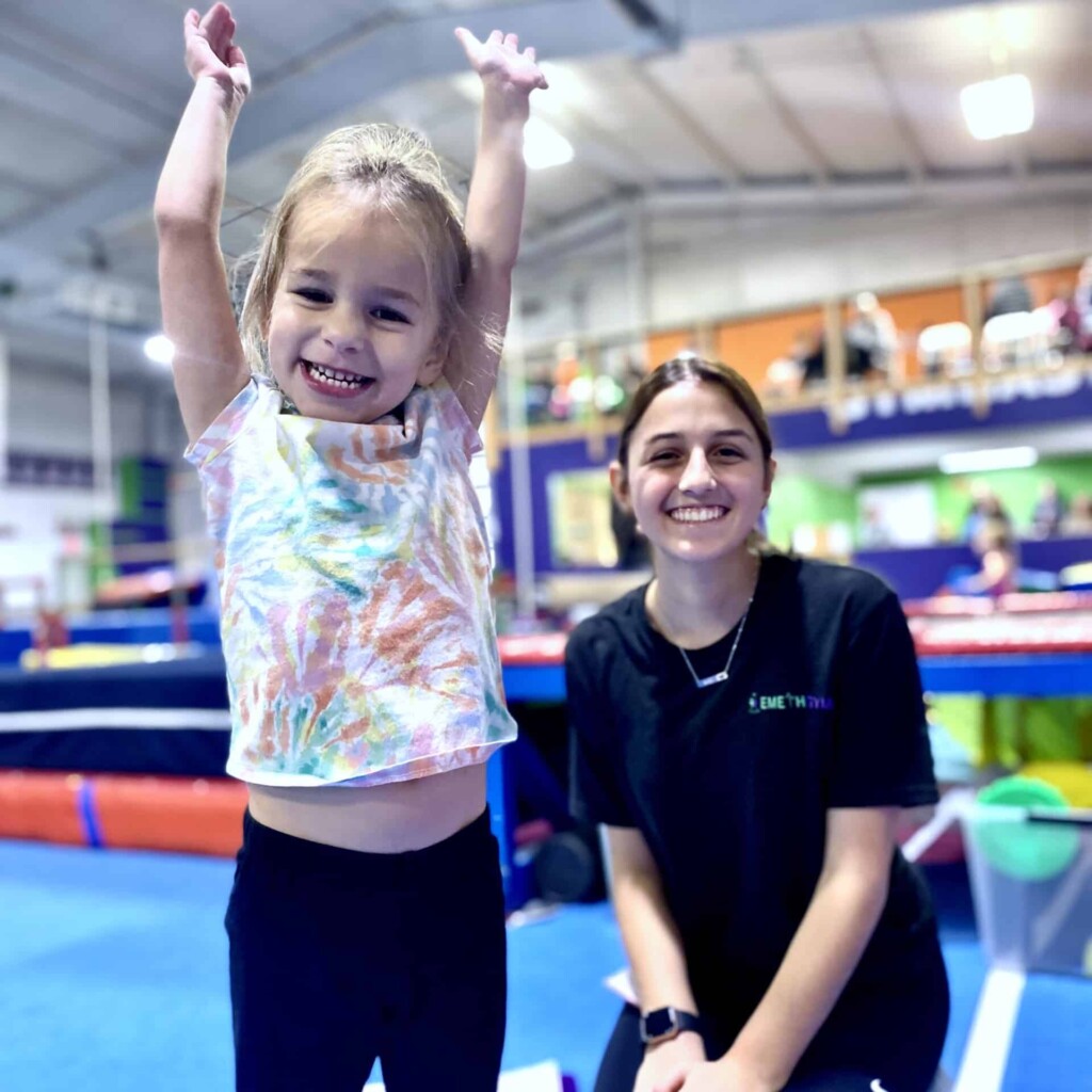 Coach with happy little girl in toddler gymnastics class Toddler teacher with student on parallel bars