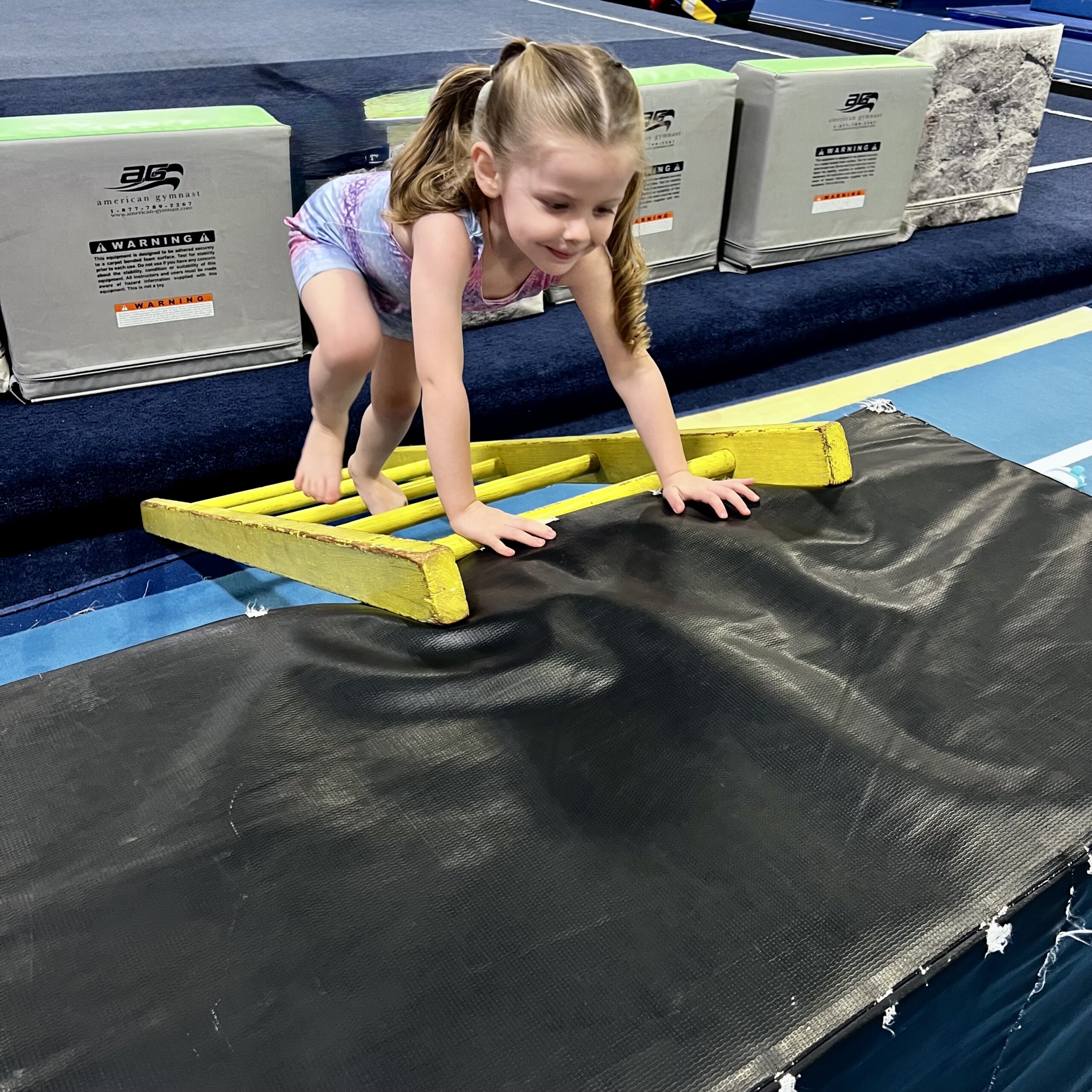 Preschool girl climbing ladder in gymnastics class Mom with toddler and preschooler in gymnastics class